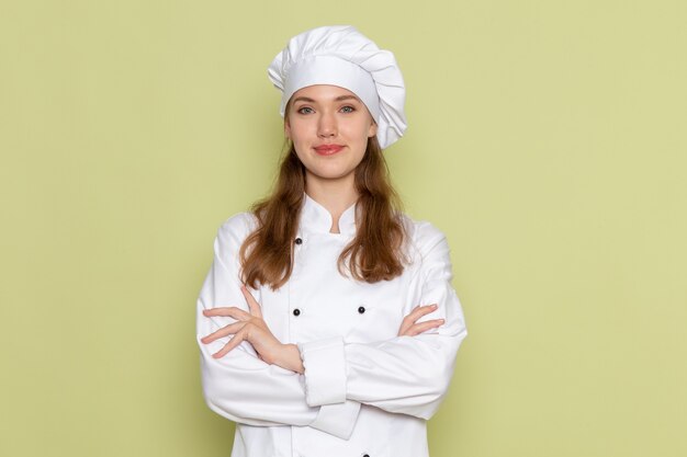 Front view of female cook in white cook suit smiling and posing on green wall