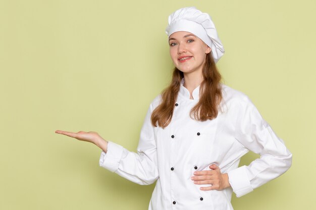 녹색 벽에 포즈 웃 고 흰색 쿡 정장 여성 요리사의 전면보기