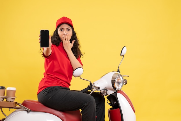 黄色の背景に電話を保持しているコーヒー配達用の自転車に乗った正面の女性宅配便サービス配達制服の仕事の女性