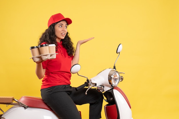 Front view female courier on bike for coffee delivery on the yellow background job service uniform worker woman delivery work