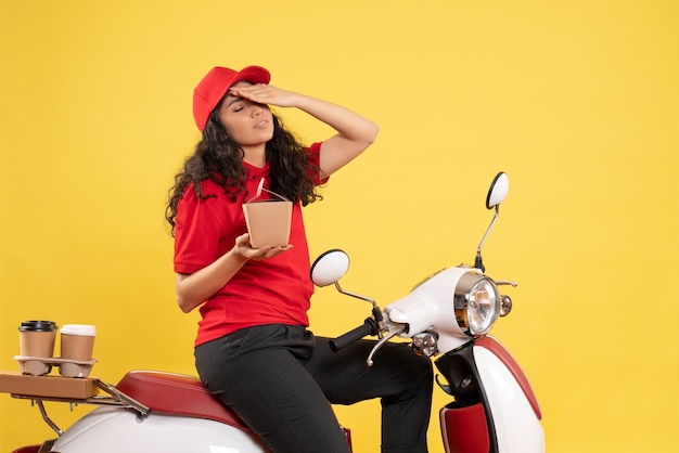 Front view female courier on bike for coffee delivery on yellow background service delivery uniform job worker woman