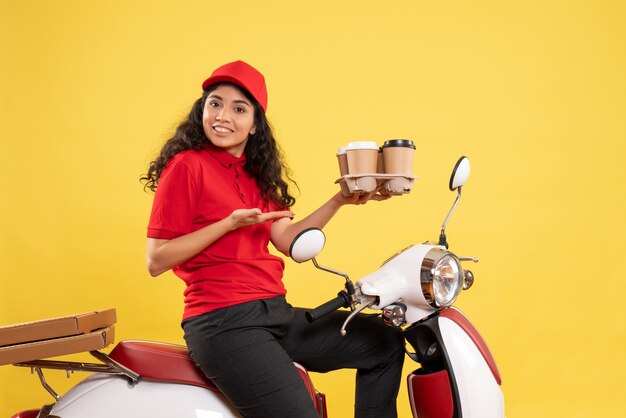 Front view female courier on bike holding coffee cups on yellow background worker service uniform job woman delivery work