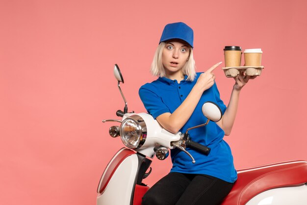 Front view female courier on bike with coffee cups on pink 