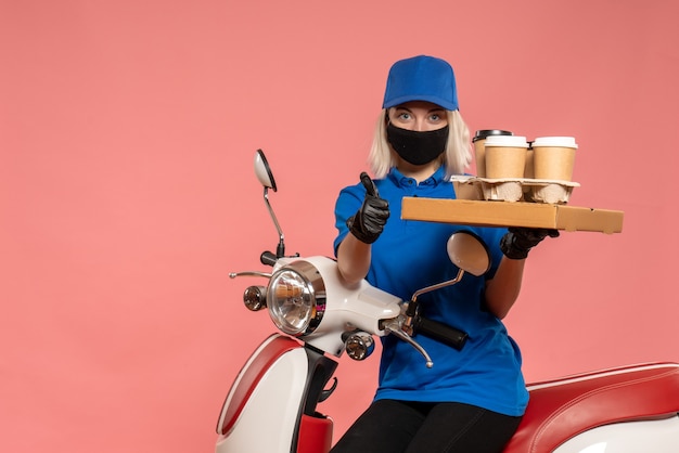 Front view female courier on bike with coffee cups on the pink 