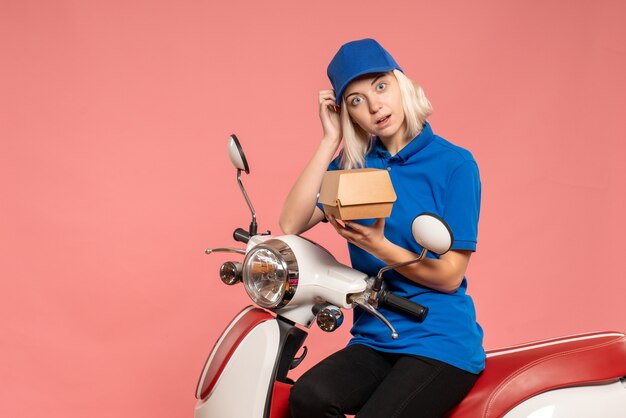 Front view female courier on bike with little food package on a pink 