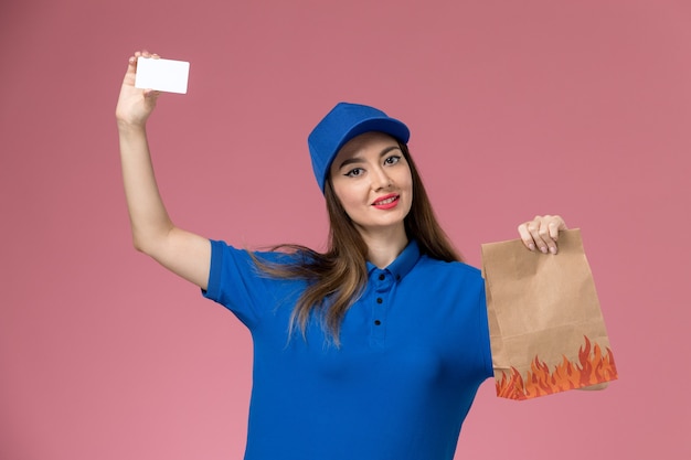 파란색 유니폼과 케이프 핑크 책상에 카드와 종이 음식 패키지를 들고 전면보기 여성 택배