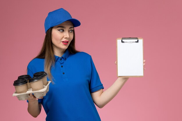 ピンクの壁にコーヒーカップとメモ帳を保持している青い制服と岬の正面図の女性の宅配便