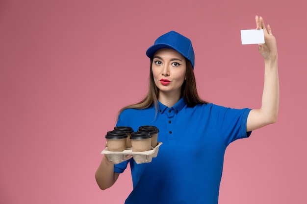 Corriere femminile di vista frontale in uniforme blu e mantello che tiene tazze di caffè e carta bianca sul muratore rosa