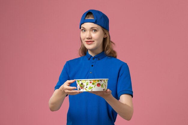 분홍색 벽, 서비스 배달 작업자 직원에 배달 그릇을 들고 파란색 유니폼 케이프에서 전면보기 여성 택배