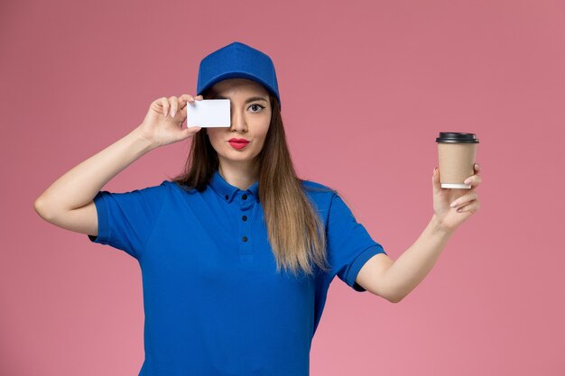 파란색 유니폼과 케이프 핑크 책상 작업에 배달 커피 컵과 흰색 카드를 들고 전면보기 여성 택배