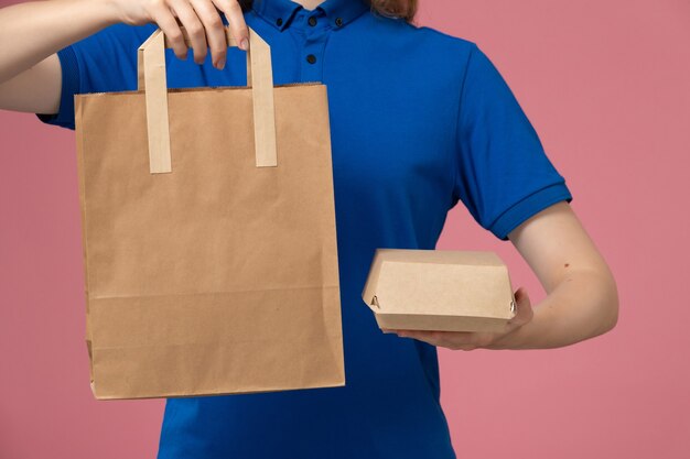 Женщина-курьер в синей форме, держащая посылки на розовой стене, служба доставки сотрудников