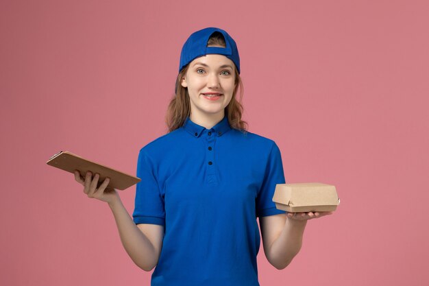 분홍색 벽, 소녀 배달 서비스 직원에 작은 배달 음식 패키지와 메모장을 들고 파란색 유니폼과 케이프 전면보기 여성 택배