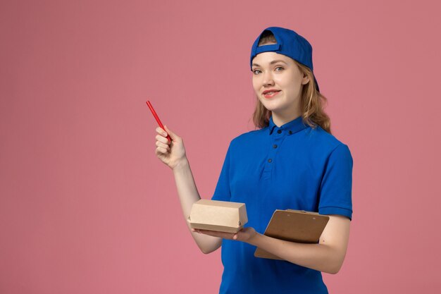 Женщина-курьер в синей униформе и плаще, держащая небольшой блокнот для доставки еды и пишущий на розовой стене, сотрудник службы доставки вакансий