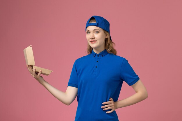 파란색 유니폼과 분홍색 벽에 작은 배달 음식 패키지를 들고 케이프 전면보기 여성 택배, 배달 유니폼 서비스 작업 직원