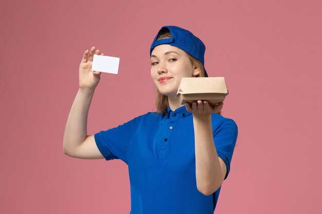 Женщина-курьер в синей униформе и накидке с карточкой на розовой стене, вид спереди, работник службы доставки