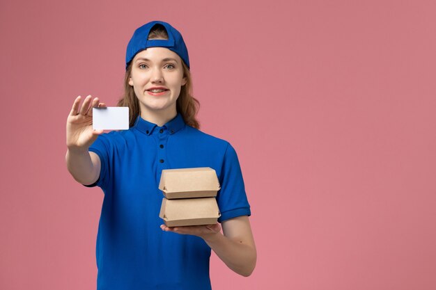 Вид спереди женщина-курьер в синей униформе с маленькими пакетами с едой и карточкой на розовом фоне работа сотрудника службы доставки