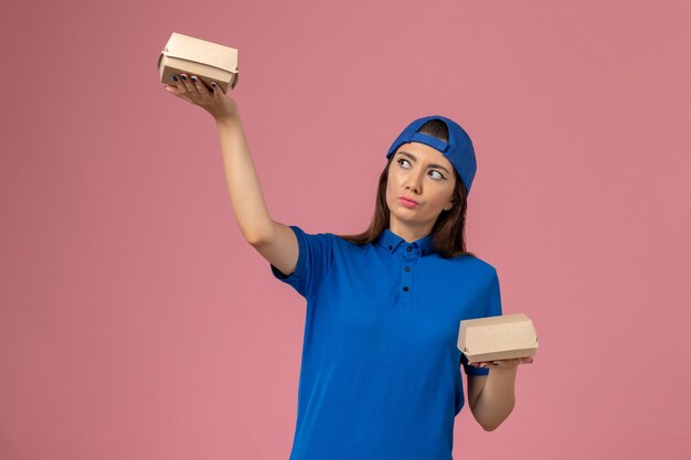 분홍색 벽, 직원 서비스 배달 노동자에 작은 배달 패키지를 들고 파란색 유니폼 케이프 전면보기 여성 택배