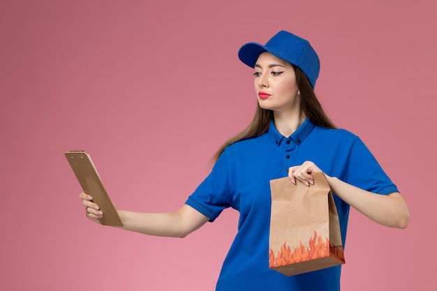 ピンクの壁にメモ帳の紙の食品パッケージを保持している青い制服と岬の正面図の女性の宅配便