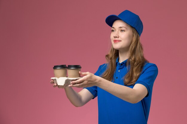 회사 작업을 제공하는 분홍색 배경 서비스 유니폼에 갈색 커피 컵을 제공하는 파란색 유니폼에 전면보기 여성 택배
