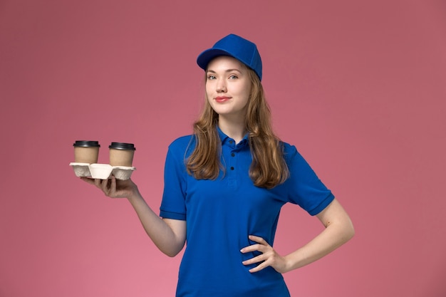 핑크 데스크 서비스 유니폼 제공 회사에 포즈 갈색 커피 컵을 들고 파란색 유니폼에 전면보기 여성 택배