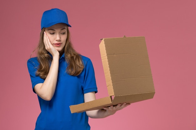 Front view female courier in blue uniform holding empty food delivery box on pink desk worker service uniform company job