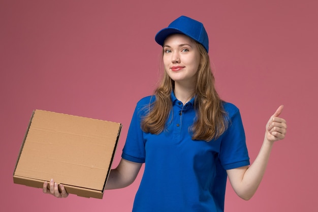 Front view female courier in blue uniform holding food box on pink background job service uniform company