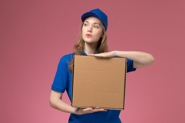 Front view female courier in blue uniform holding food delivery box on pink background service uniform company