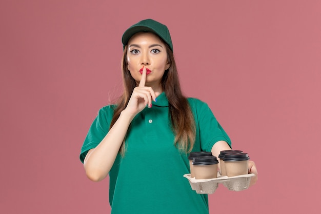 緑の制服を着た正面図の女性の宅配便と淡いピンクの壁サービスの制服配達の仕事で配達コーヒーカップを保持している岬