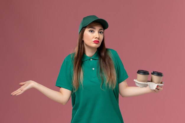 녹색 유니폼과 케이프 핑크 벽에 배달 커피 컵을 들고 전면보기 여성 택배 회사 서비스 작업 유니폼 배달 작업자 작업 소녀