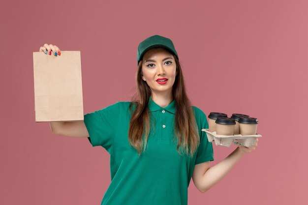 緑の制服を着た正面図の女性の宅配便とピンクのデスクサービスの制服配達仕事の女の子に食品パッケージと配達コーヒーカップを保持している岬