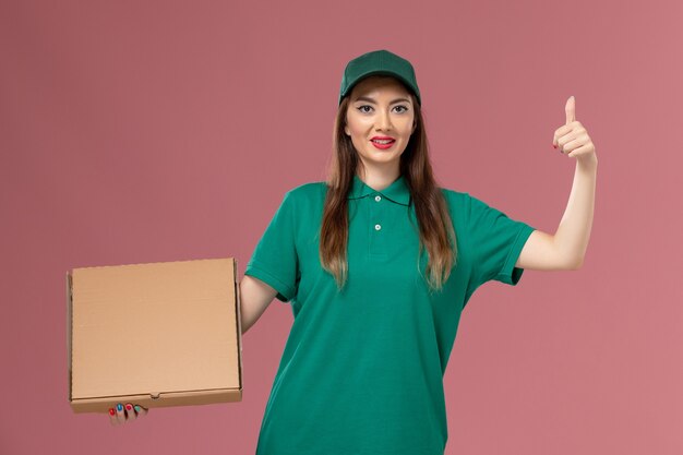 ピンクの壁にフードボックスを保持している緑の制服を着た正面図の女性の宅配便