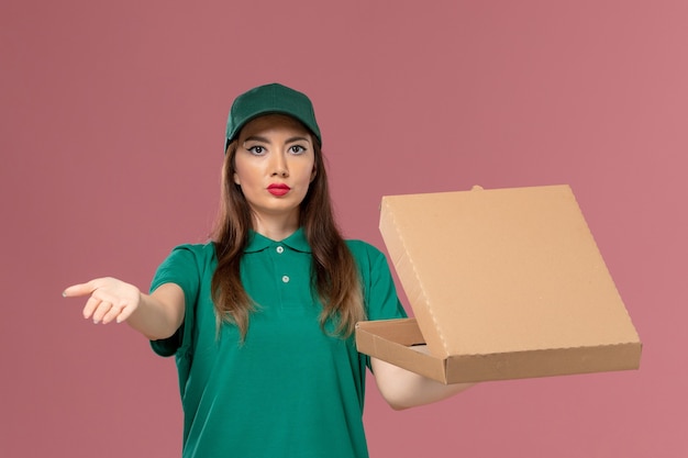 Front view female courier in green uniform holding food delivery box on pink wall company job service uniform work delivery