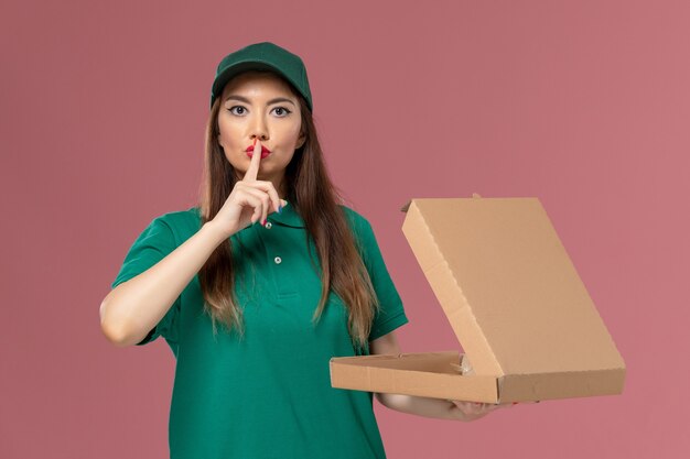 Front view female courier in green uniform holding food delivery box on pink wall company service uniform delivery job