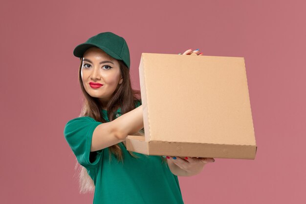 분홍색 벽 회사 서비스 유니폼 배달 노동자에 음식 배달 상자를 들고 녹색 제복을 입은 전면보기 여성 택배