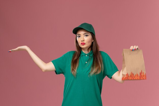 ピンクの壁のサービスの制服の配達に食品パッケージを保持している緑の制服の正面図の女性の宅配便