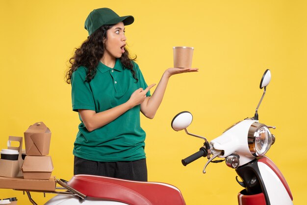 Front view female courier in green uniform with dessert on a yellow background work color job delivery woman service worker food
