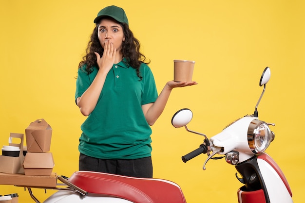 Front view female courier in green uniform with dessert on yellow background work color job delivery woman worker food