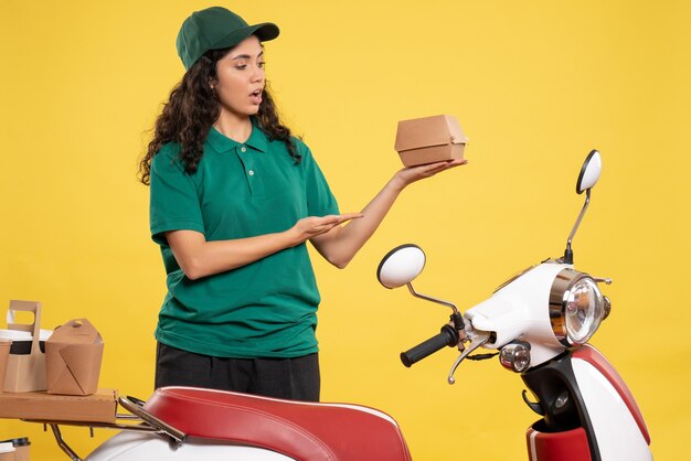 Вид спереди женщина-курьер в зеленой униформе с маленьким пакетом продуктов на желтом фоне рабочий цвет работа доставка еда женщина работник службы