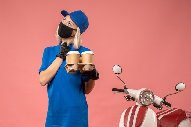 Front view female courier holding coffee cups on pink 