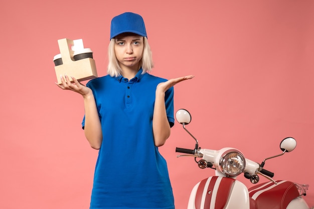 Front view female courier holding coffee on pink 