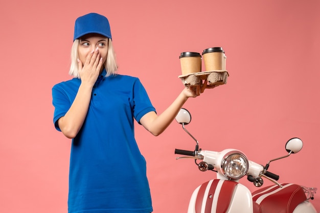 Front view female courier holding delivery coffee on pink 