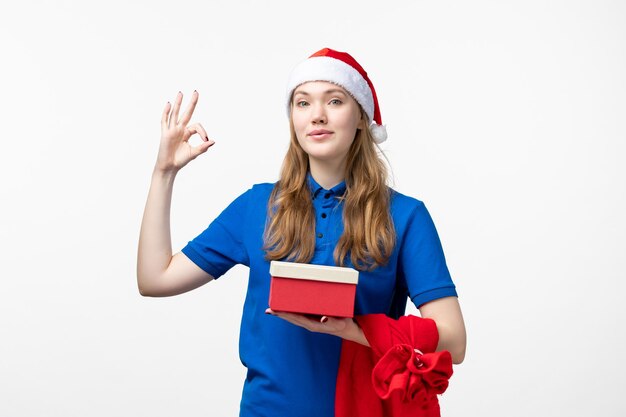 Front view of female courier holding holiday present on white wall