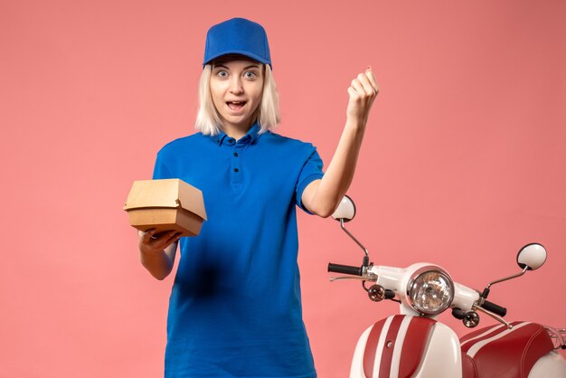 Front view female courier holding little food package on pink 