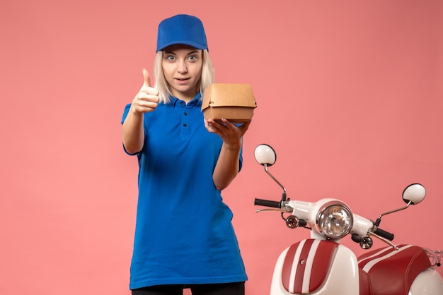 Front view female courier holding little food package on the pink 