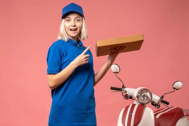 Front view female courier holding pizza box on pink 