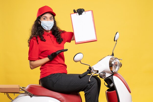 Foto gratuita corriere femminile vista frontale in maschera con nota di file su sfondo giallo covid- consegna di lavoro uniforme servizio di lavoro del lavoratore pandemia