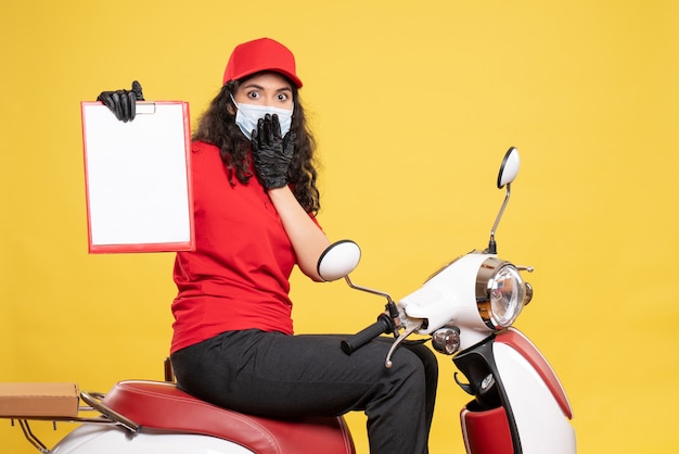 Front view female courier in mask holding file note on yellow background covid- job uniform service work pandemic delivery