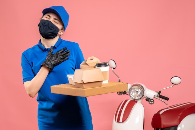 Front view female courier in mask with delivery coffee and food on pink 