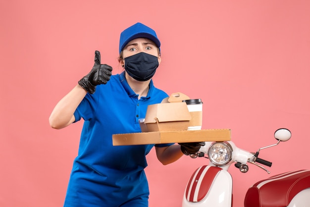 Front view female courier in mask with delivery coffee and food on pink 