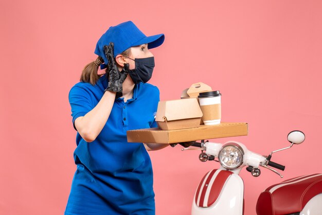 Front view female courier in mask with delivery coffee and food on pink 